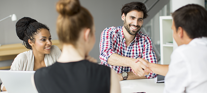 V1_Work_Cross_Fuctionally_Innovation_NuSkin_compressed a group of people in a meeting look over at two men shaking hands.