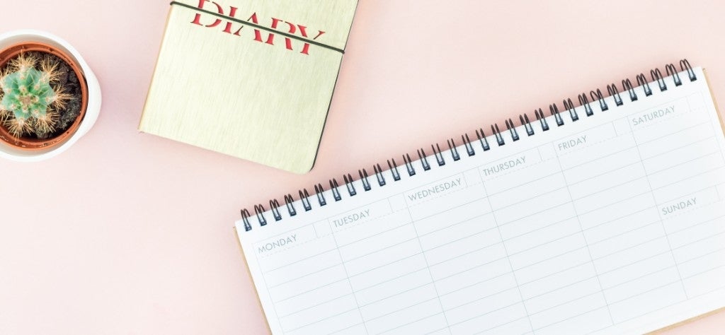 Top view of office workspace desk diary and weeklong calendar